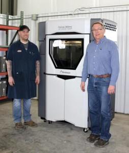 Scott Fortune (right) and his son Alex (left) stand beside the new state-of-the-art 3D printer they purchased to expand on services offered at Upper Iowa Tool & Die.
